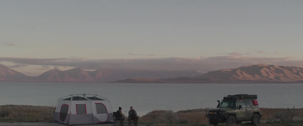 Two men camp near a large body of water