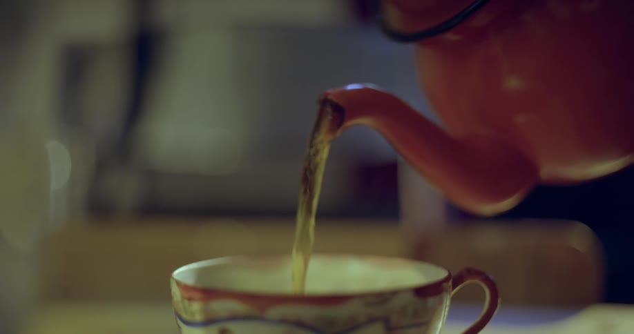 Person pours tea from teapot into a china teacup, steam rises up