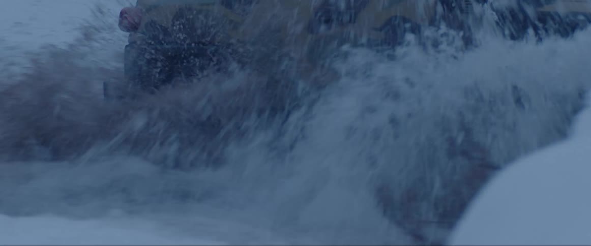 Vehicle splashes water while driving through river in snow covered terrain as snow falls