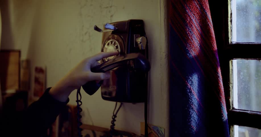Medium close up of a hand picking up a receiver of an old fashioned phone and dialling