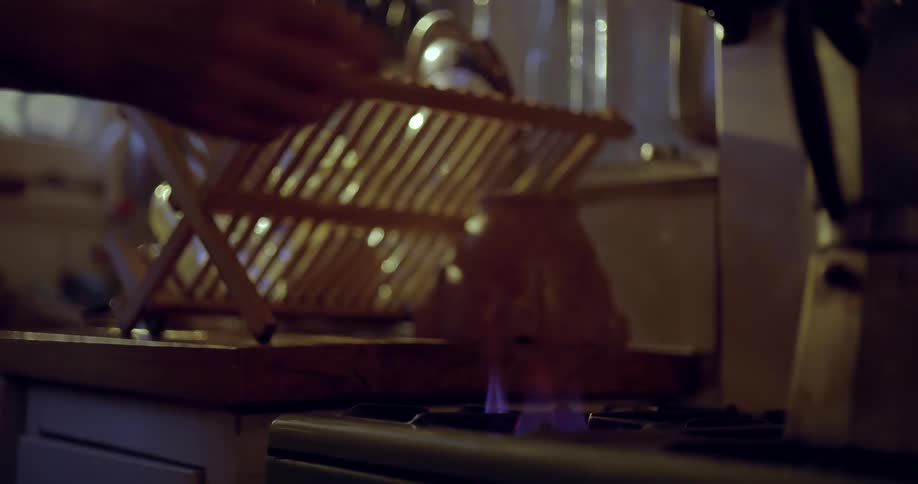 Medium close up of someone striking a match, lighting a gas stove and placing a coffee pot over the flame