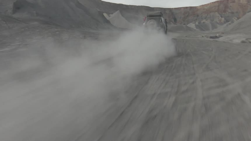 Vehicles moving fast on a sandy road between hills at daytime