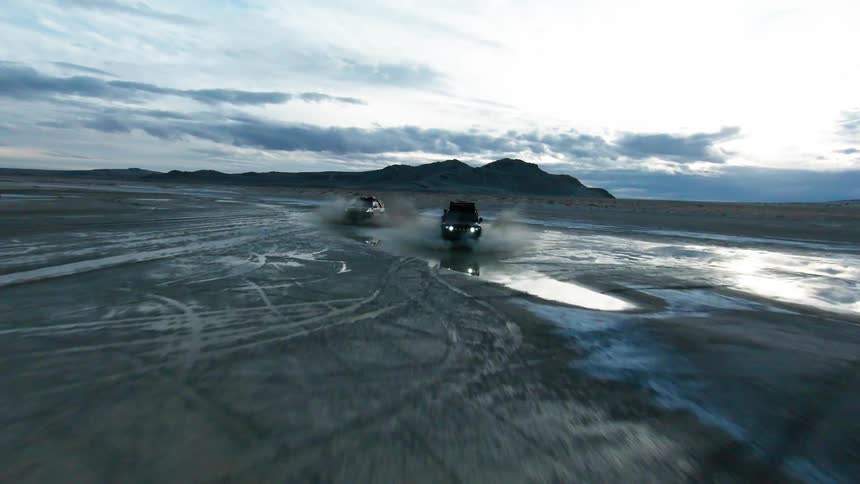 Two jeeps passing at high speed over desert soil splashing water