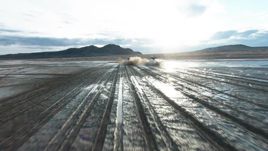 Two pickup trucks at very high speed passing through desert soil with clay