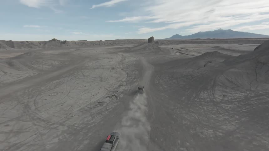 Vehicles driving along dirt road through arid hills create a trail of dust