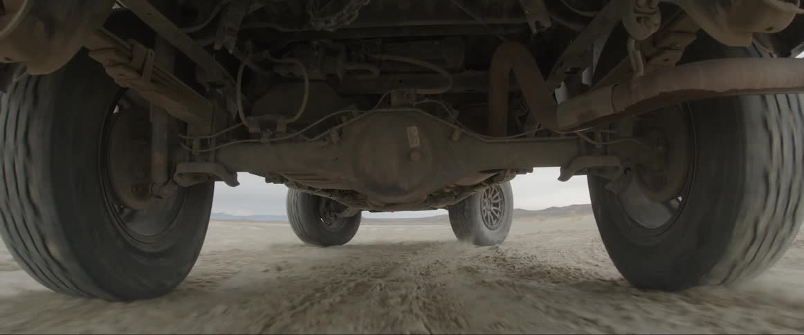 Underside of a moving vehicle kicking up dust on a dry dirt road