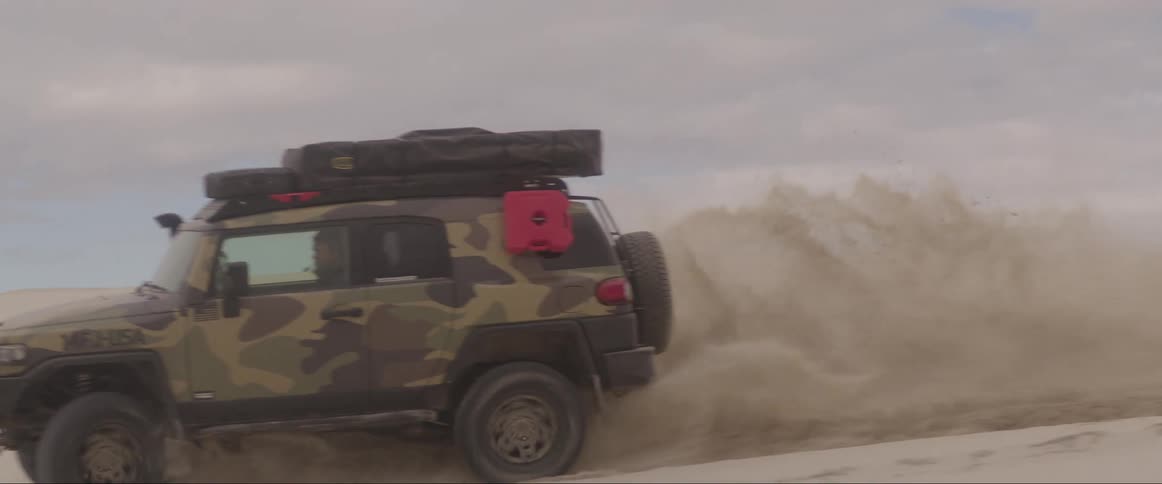An off road vehicle kick dust driving over a sand dune