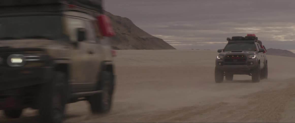 Two pickup trucks traveling on desert soil on a cloudy morning