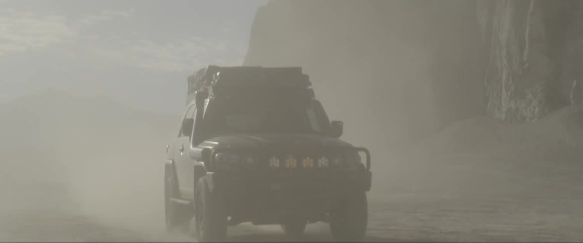 A large jeep drives swiftly along a very dusty desert canyon