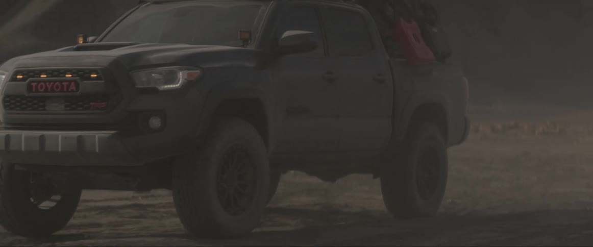 A pickup truck drives on a rocky terrain with large rocks in the background