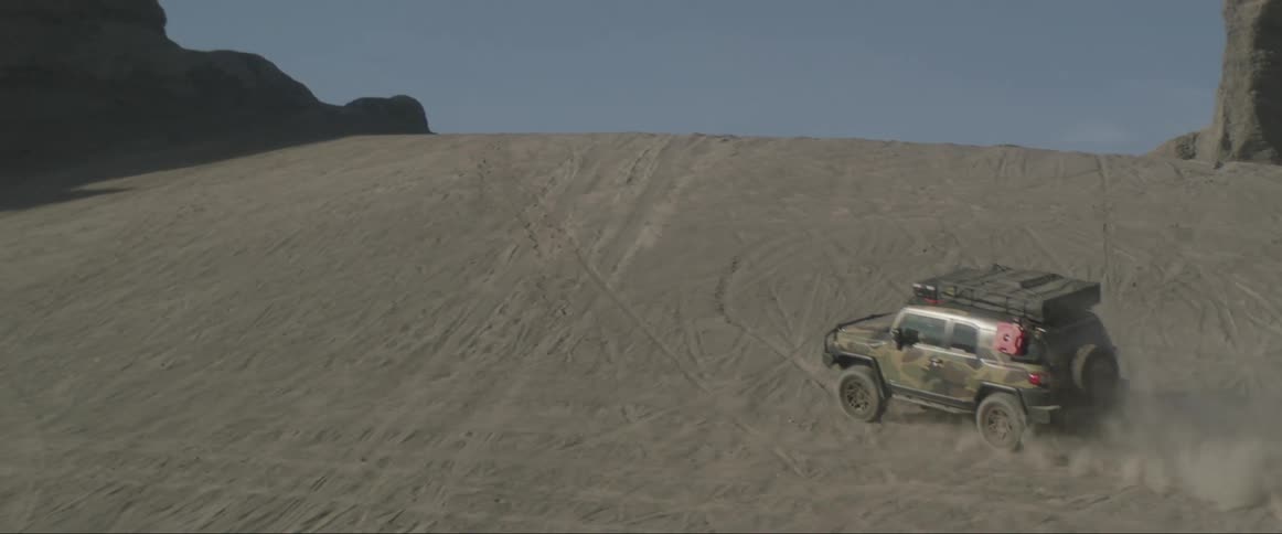 Jeep traveling across desert soil and getting dusty when climbing a small hill performing a maneuver