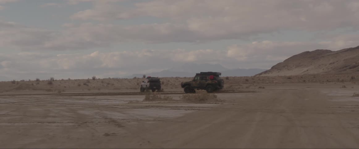 Two vehicles performing stunts on a sandy road at midday