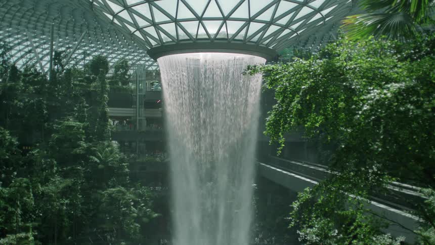 Inside a greenhouse with trees plants and water falling from the ceiling down in a modern way