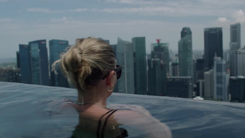 Woman inside a swimming pool of a building with a panoramic view of a metropolis with a skyscraper