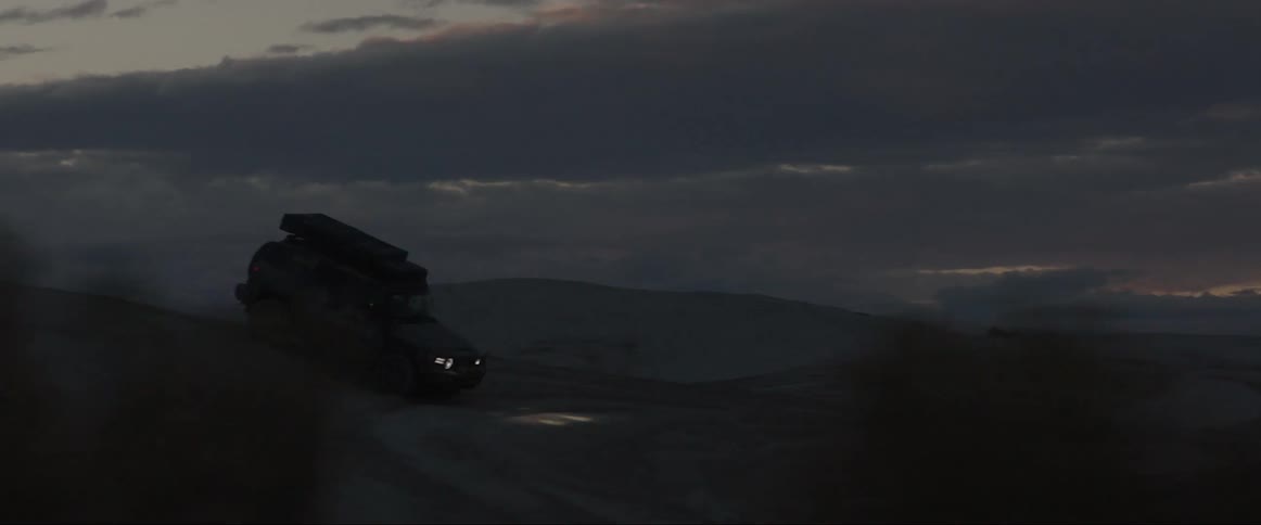Silhouette of a sports pickup truck descending a hill in a dark dawn sky