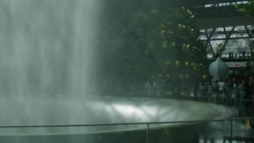 Family passes large interior water fountain in busy shopping mall
