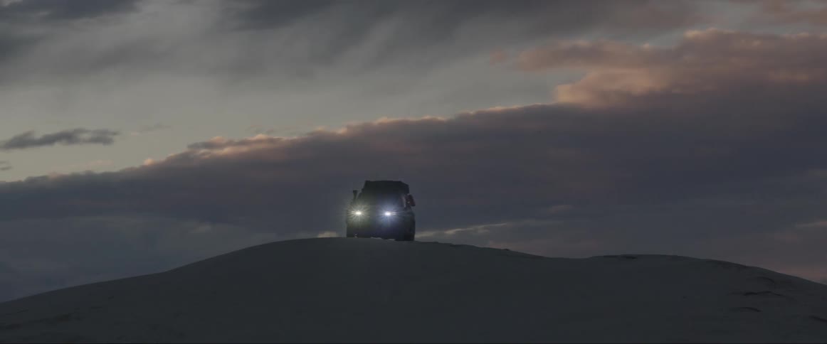 A person boards a solitary car on a sand dune at sunset
