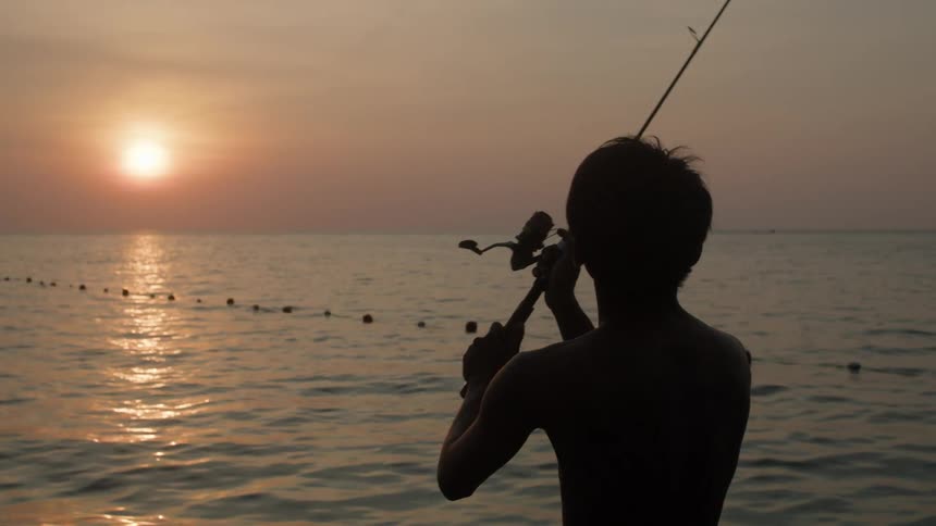Boy casting a fishing rod into the sea on a late afternoon with a sunset on the horizon