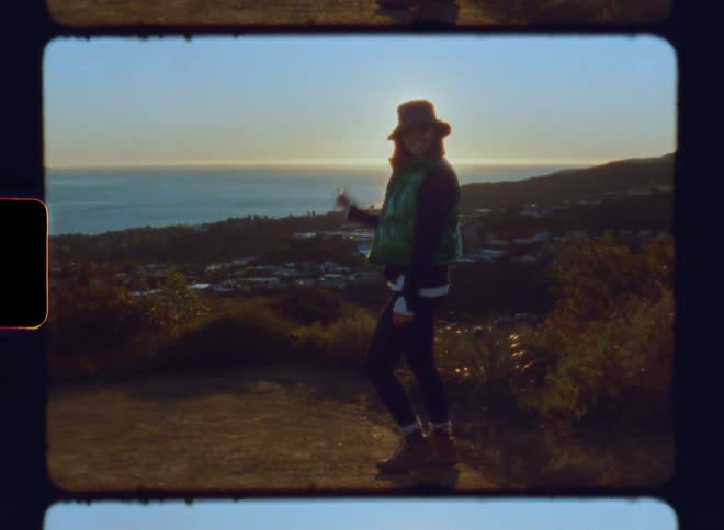 Woman on a mountain peak waving goodbye with a panoramic view of a city and the sea