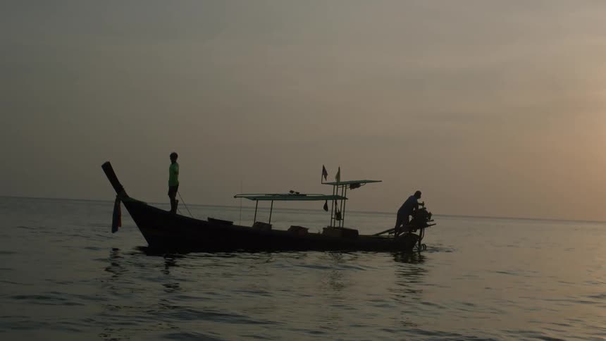 Man operating a wooden boat on the water at sunset while the child stand on the other end