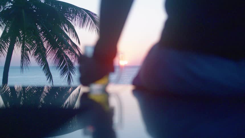 Person sitting drinking a glass of beer with a view of the sea and the sunset on the horizon