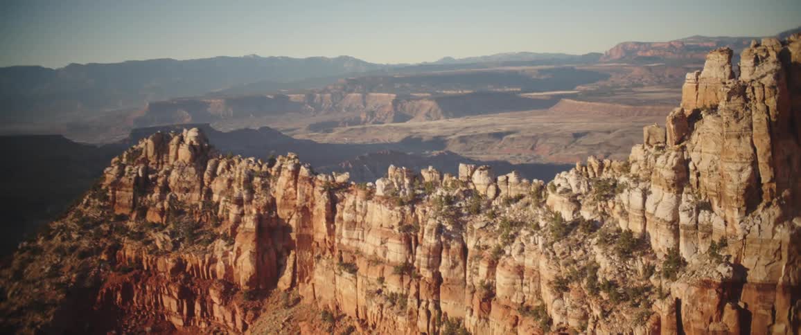 Vegetation dotted ridge towers over foggy arid rough terrain