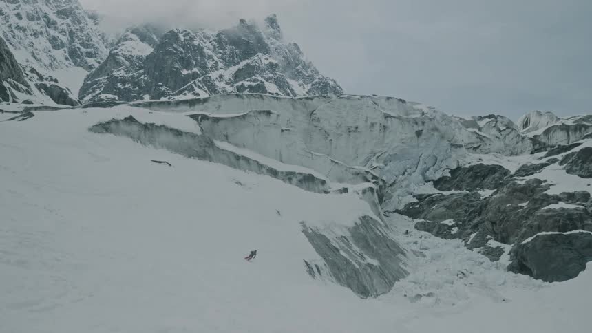Snow skier riding a glacier with cloud covered peaks in the background
