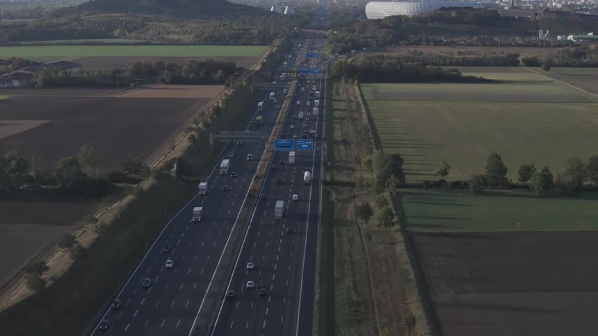 Aerial panorama over munich of a highway with traffic and fields and access to a city with wind energy