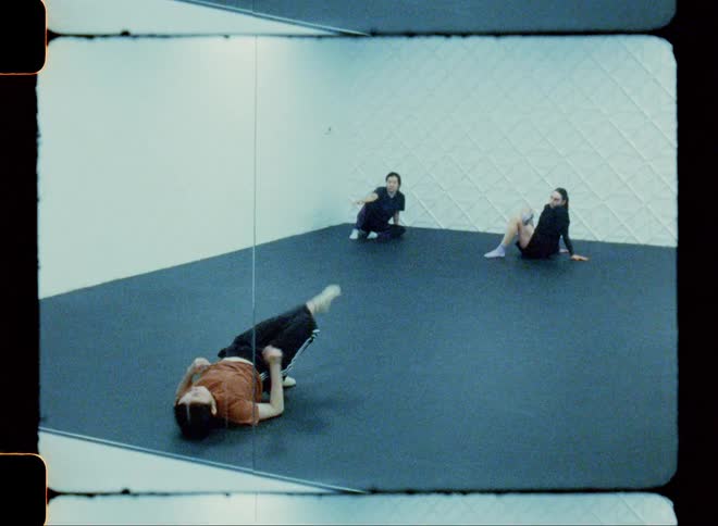 A teen break dancing on the floor indoor while two other teens watch