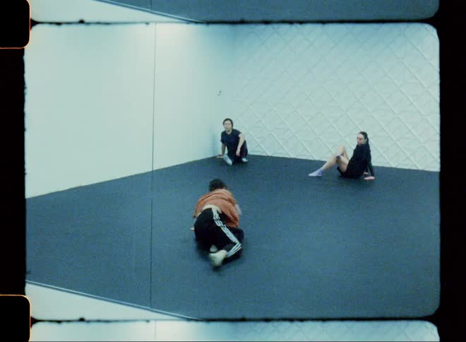 Woman dancing in front of a studio mirror and two other people sitting watching her