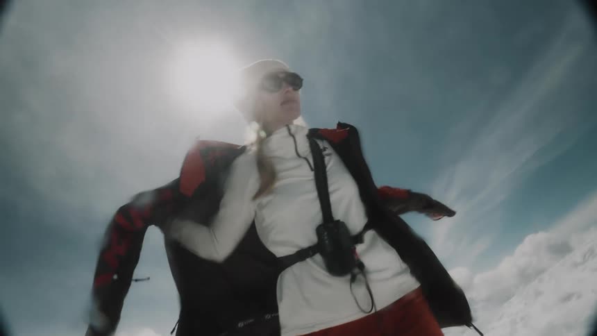 Woman putting on a cold jacket while standing on the hill of a mountain covered in snow