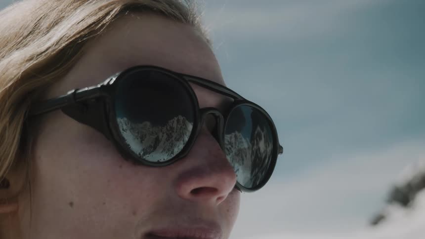 Portrait of a blonde woman wearing black sunglasses amid snowcovered mountains