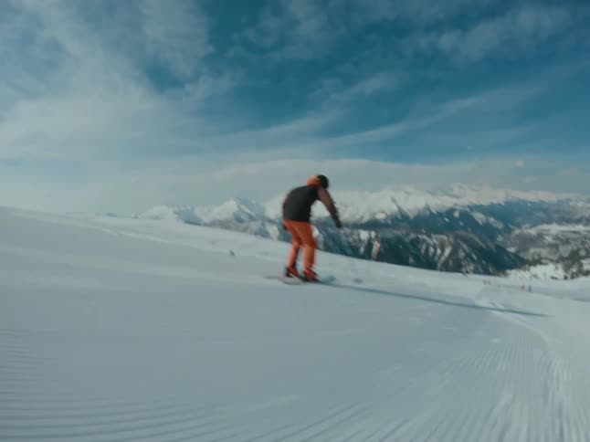 Rider skiing down a snowy slope on a bright day with mountains and blue sky in the background