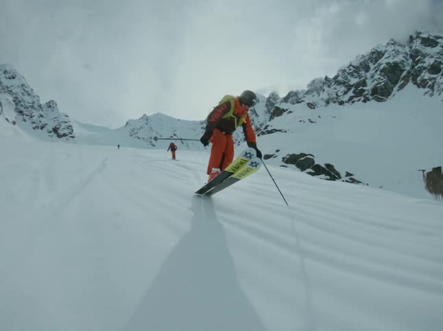 A riders in orange clothes is skiing down a freeride mountain