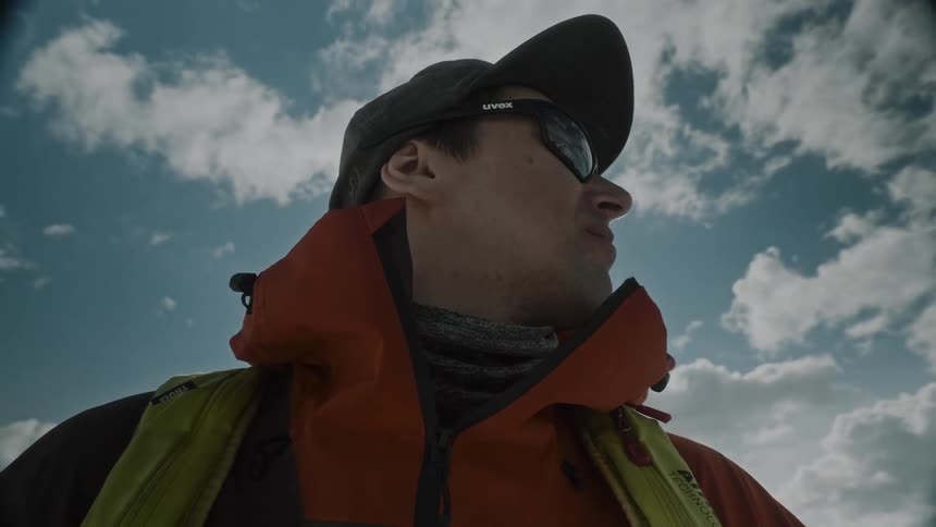Close up of a man wearing sunglasses and an orange jacket under a blue sky