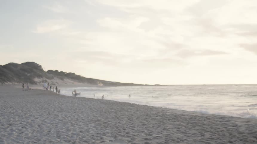 People playing on the beach as waves crash into the shoreline on a cloudy white under a white sky