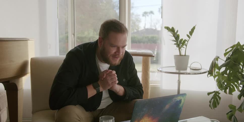 Man sitting in an armchair and having a conversation with someone through the laptop