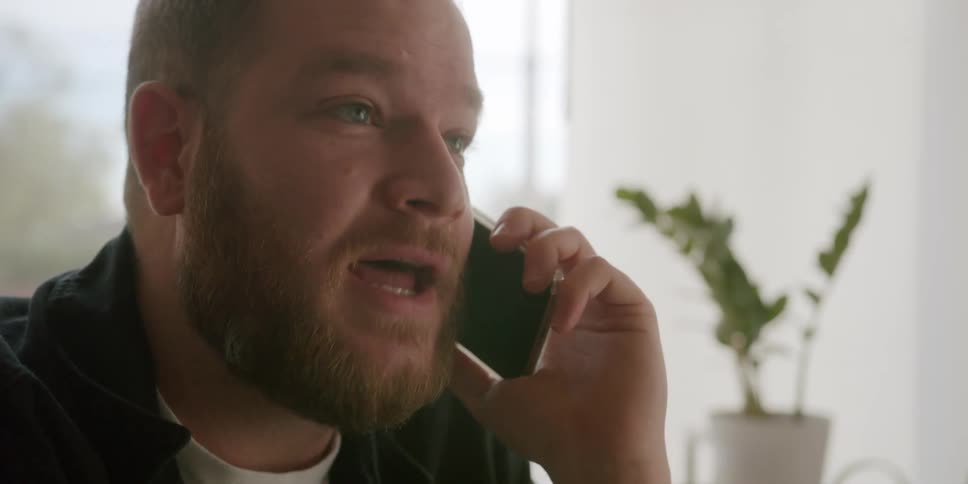A man sitting in a room talking on a smartphone