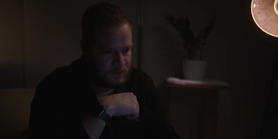 Man sitting on a dimly lit living room working on a computer or laptop