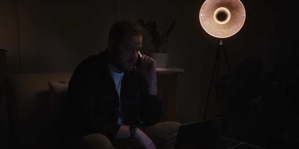 Man sitting on the couch in a dark room talking on the phone