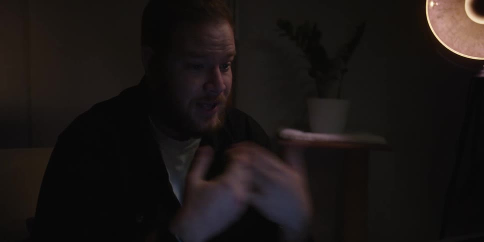 Portrait of a man sitting in a dimly lit room talking and gesturing with his hands