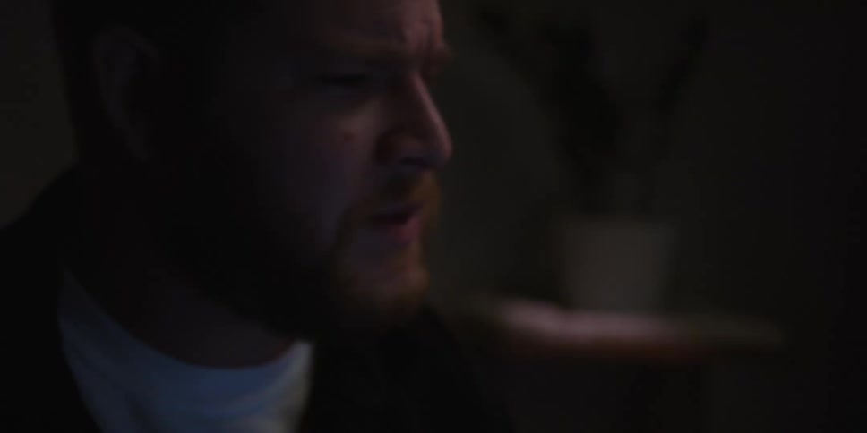 Close up of the face of an upset bearded man arguing in a dimly lit room