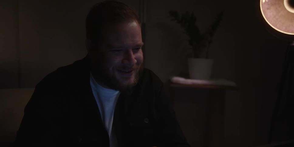 Portrait of a man sitting on a sofa in a dark room talking with worried facial expression
