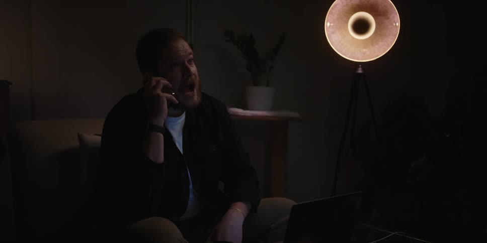 Man sitting on a dimly lit living room impatiently waiting for a call