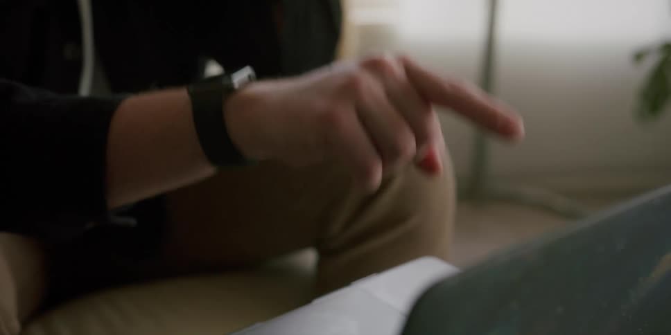 A man sitting down in a room talks on the phone and gestures at a laptop