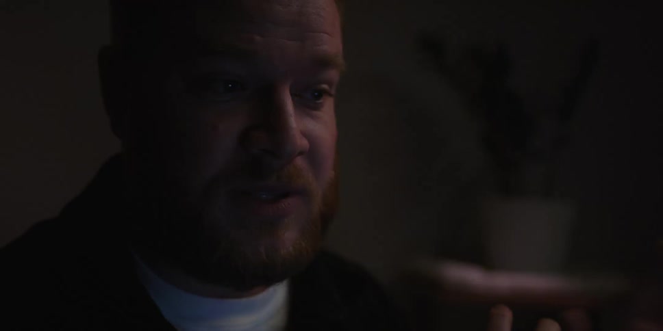 Portrait of a man with a beard talking and gesturing his hands in a room with low lighting
