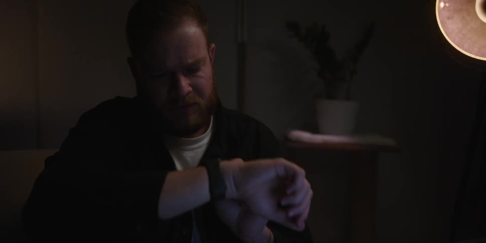 Portrait of a man sitting in a dark room sending a message with his apple watch and with a worried facial expression