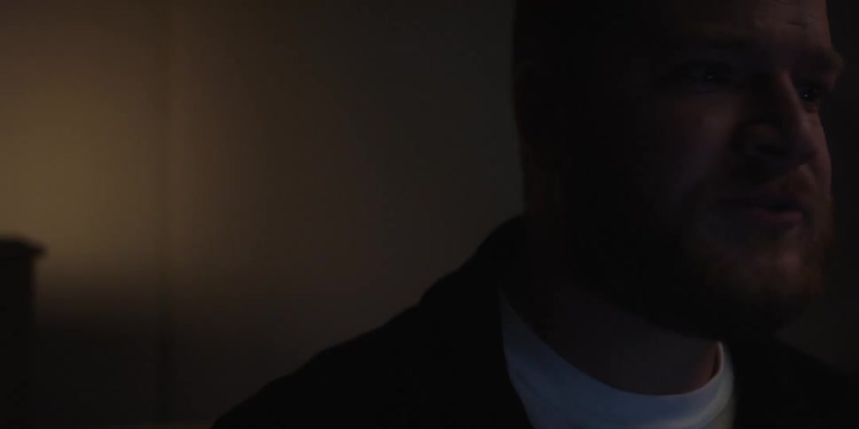 Close up of a bearded man talking on a dimly lit room