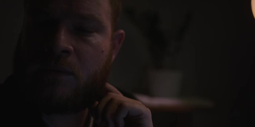 A bearded man pauses to ponder something while stroking his beard