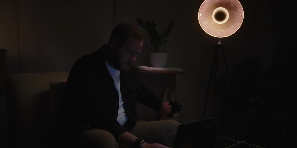 A man pets his cat and looks at his laptop